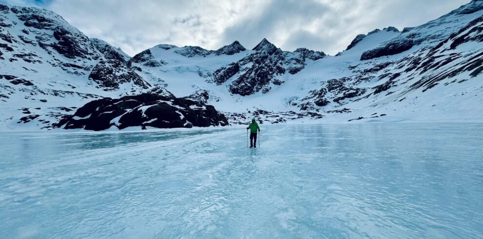 Persona caminando sobre la Laguna de los Témpanos congelada en Ushuaia, rodeada de imponentes montañas.