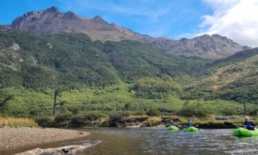 Experiencia de packrafting con XPLOR Turismo en Ushuaia, Argentina. Tres remeros en kayaks inflables verdes en un río con montañas y bosques de Tierra del Fuego al fondo.